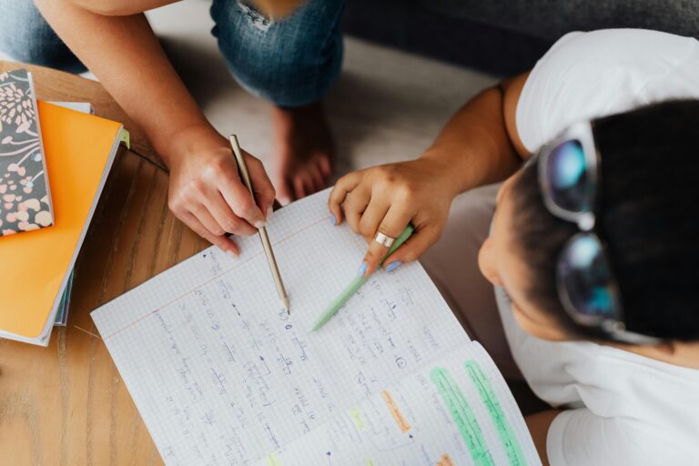 Two students studying together with notebooks and pens, viewed from above.